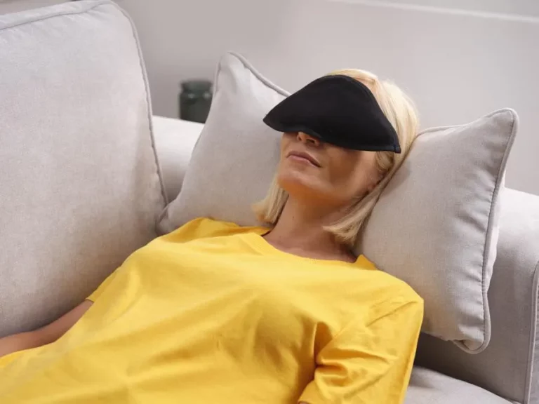 Auf der Couch liegende Frau, die eine wärmende Augenmaske trägt.